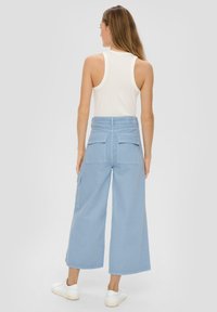 Hellblaue weite Hosen aus robuster Fabric mit zwei Gesäßtaschen und einer seitlichen Tasche, kombiniert mit einem eng anliegenden weißen Tanktop und weißen Sneakers.