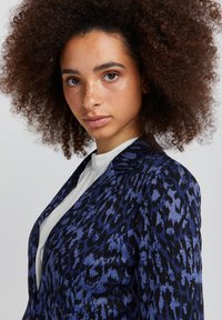 Blå og sort leopardprint blazer med en tætsiddende design. Stof med en blød tekstur og stiklapper, suppleret af en hvid bluse.