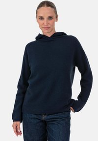 Pull à capuche bleu marine avec une texture douce et une coupe ample, doté de manches longues et d'un ourlet côtelé, associé à un jean foncé.