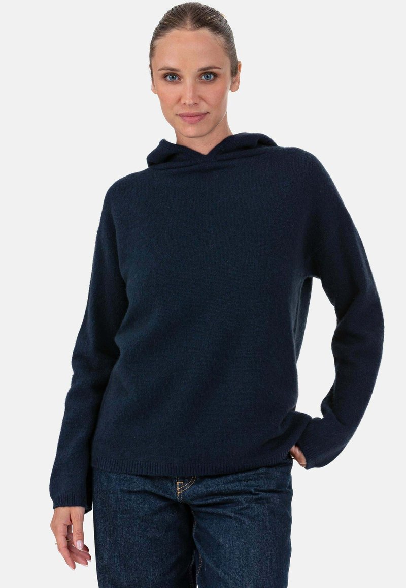 Pull à capuche bleu marine avec une texture douce et une coupe ample, doté de manches longues et d'un ourlet côtelé, associé à un jean foncé.