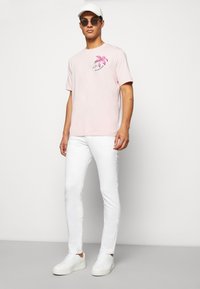 Lyserød bomulds t-shirt med blomsterprint på venstre bryst. Sammen med hvide tætsiddende jeans og hvide sneakers.