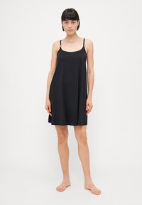 Vestido negro sin mangas con tirantes ajustables, tejido suave, forma en A, altura a la rodilla, diseño minimalista y sin patrones ni adornos visibles.