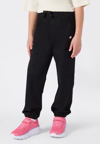 Pantalones deportivos negros con puños elásticos y cintura con cordón, que cuentan con bolsillos laterales y un pequeño logo en el muslo izquierdo.