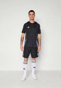 Černé atletické tričko se zelenými a fialovými akcenty, doplněné černými šortkami, bílými ponožkami s černými pruhy a bílými kopačkami.