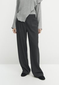 Donkergrijze, wijde broek met subtiele streepjes. Gepaard met een lichtgrijze, gestructureerde top met lange mouwen die een gelaagd ontwerp heeft.