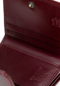 Il portafoglio in pelle bordeaux presenta all'interno diversi scomparti per carte e una chiusura a scatto. Superficie testurizzata con dettaglio del logo in rilievo.