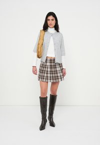 Γκρι ζακέτα με κοντά μανίκια, λευκό ζιβάγκο, καρό φούστα A-line σε καφέ τόνους και καφέ μπότες μέχρι το γόνατο. Καφέ σατέν τσάντα κρεμασμένη στον ώμο.