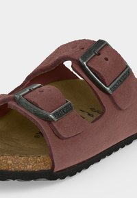 Κοντινή εικόνα ενός ροζ σανδάλου Birkenstock με δύο ρυθμιζόμενες μαύρες μεταλλικές αγκράφες και φελλό πάτο σε μαύρη σόλα.