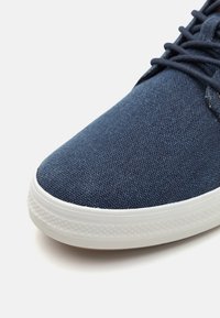 Dark blue canvas sneaker with a smooth texture, white rubber sole, and black laces. Rounded toe with a simple design and reinforced stitching.