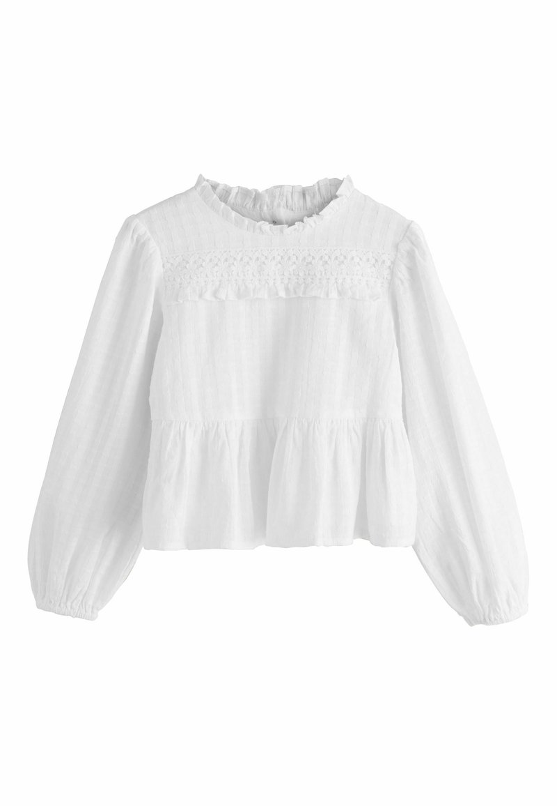 Blusa peplum blanca con mangas largas y cuello con volantes. Presenta un tejido texturizado y una franja de encaje decorativo en el pecho.
