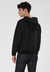 Schwarzer Hoodie mit geräumigem R�ücken und angenommener Kapuze, ausgestattet mit gerippten Bündchen und Saum. Glatte Textur, die ein minimalistisches Design zur Schau stellt.