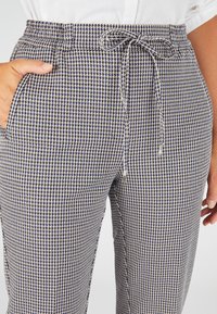 Karierte, hochtaillierte Hose in Marineblau und Beige, mit einem Kordelzugbund, Seitentaschen und einem leichten, strukturierten Stoff.