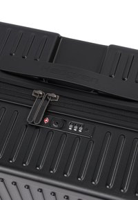 Valise rigide noire avec fermeture éclair et serrure à combinaison TSA intégrée, avec une poignée étiquetée "Hedgren" sur fond blanc.