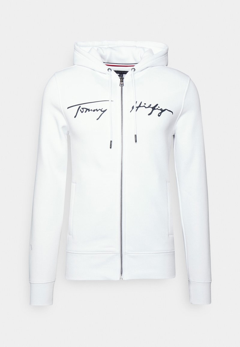 Sudadera blanca con cremallera, hecha de una tela suave, que presenta un logo negro, capucha con cordón y bolsillos laterales; textura lisa con puños acanalados.