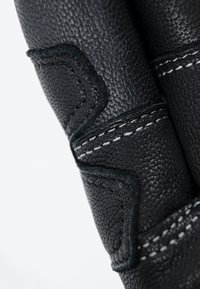 Nahaufnahme von einem schwarzen Lederhandschuh, der das strukturierte Material, die kontrastierenden weißen Nähte und die markanten Steppen zeigt.