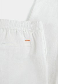 Weiße Leinenhose mit elastischem Bund, ausgestattet mit einer Gesäßtasche und einem kleinen, orangefarbenen gestickten Logo. Texturiertes, leichtes Material.