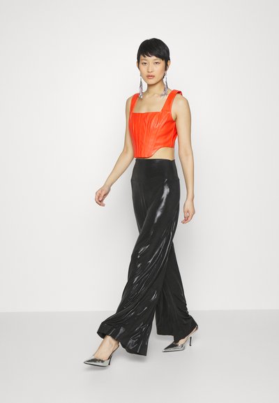 Haut court rouge avec des détails texturés, associé à un pantalon noir brillant taille haute. Le modèle porte des chaussures à talons métalliques et de longues boucles d'oreilles.