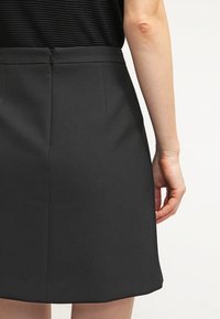 Jupe noire en tissu lisse, dotée d'une taille ajustée, d'une fermeture éclair dissimulée et de poches latérales discrètes. Design simple et minimaliste.