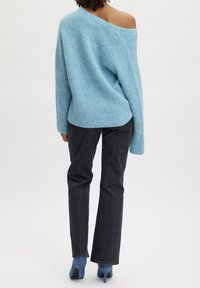 Pull bleu clair oversize à coupe ample et design épaules dénudées, associé à un jean droit en denim foncé et des chaussures à talons bleues.
