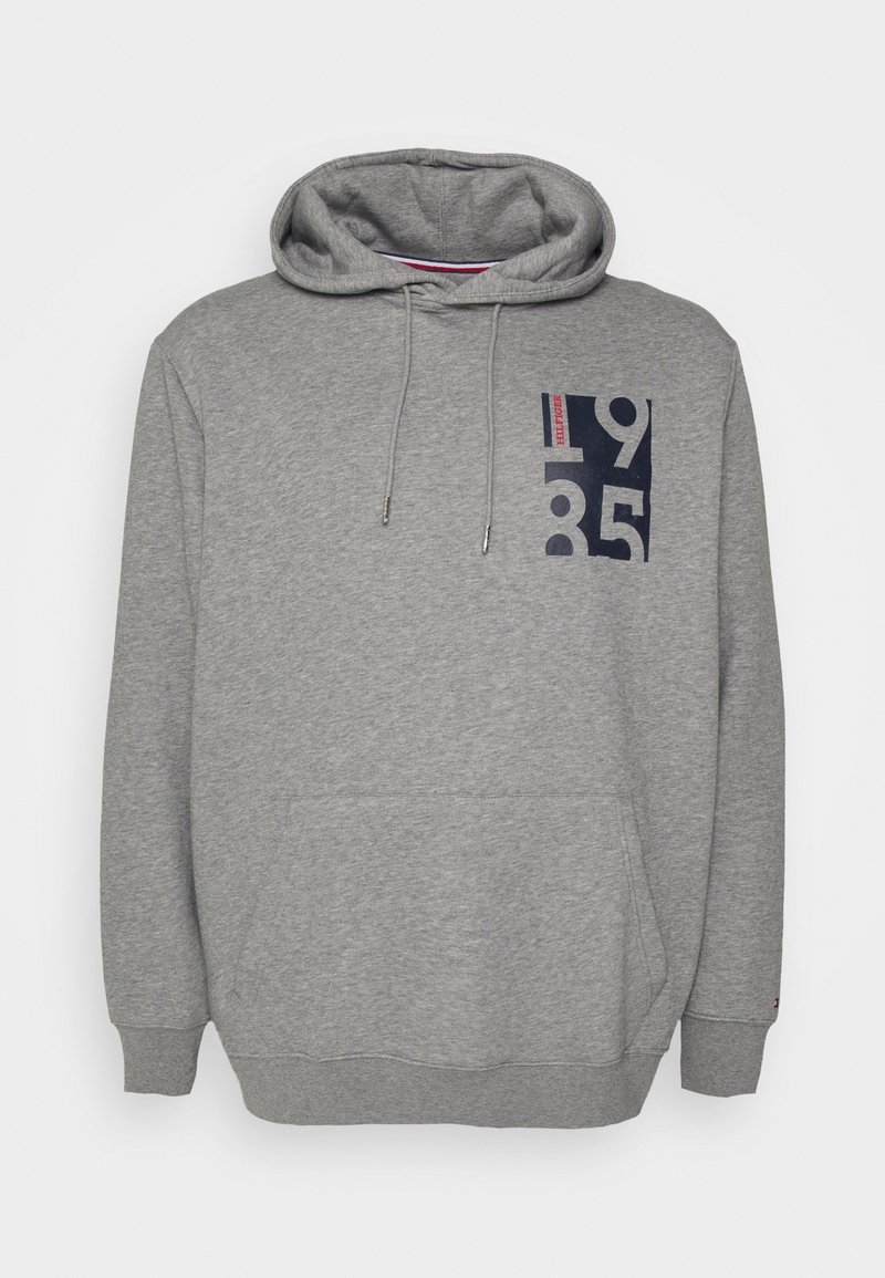 Sweat à capuche gris avec poche avant, cordons et un graphisme bleu marine "1985" avec un petit texte rouge sur le haut à gauche de la poitrine.
