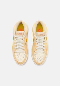 Paire de baskets beiges et blanches à lacets avec embout perforé et semelles intérieures jaune vif avec un logo soleil et basketball.