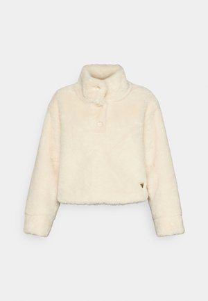 Skraťená bunda z umelého kožušiny v off-white farbe s vysokým golierom, zapínaním na gombíky a jemnou textúrou. Obsahuje logo na leme.