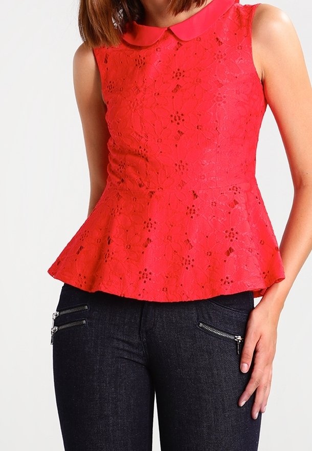 Femme portant un haut péplum en dentelle rouge sans manches avec un col et un jean foncé avec des détails zippés.