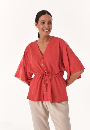 Blusa coral de botones con cuello en V, mangas cortas y anchas, y cintura con cordón. Fabricada en tela suave con una silueta relajada.
