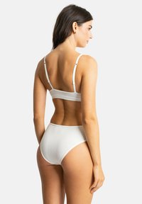 Soutien-gorge blanc à côtes et culottes taille haute, avec des fines bretelles ajustables et un design sans couture. Le matériau semble doux et texturé.