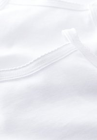 T-shirts de algodão brancas com uma textura suave, apresentando uma borda delicada em formato de ondas ao longo do decote e das cavas.