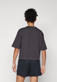 Camiseta corta de color gris oscuro con mangas cortas, que presenta un escote redondo y un acabado texturizado. Combinada con pantalones cortos de malla negros.