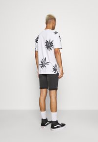 Joven con el cabello decolorado que lleva una camiseta blanca con estampados florales negros, pantalones cortos de mezclilla negros, calcetines blancos y zapatillas de caña alta negras.