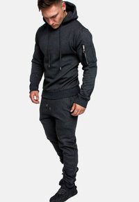 Dunkelgrauer Hoodie und Jogginghose aus weichem Stoff. Der Hoodie hat eine Kängurutasche und eine seitliche Reißverschlusstasche. Leichter, lässiger Schnitt.