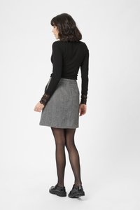 Black long-sleeve top with lace accents, paired with a gray houndstooth skirt. Model wears black tights and chunky black loafers.