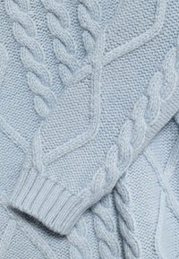 Světle modrý pletený svetr s kabelovým vzorem a zvýrazněnými copánky, s žebrovanými manžetami a texturovaným povrchem. Měkký a útulný materiál.