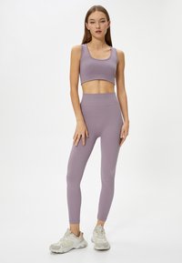 Polstret sports-bh og højtaljede leggings i lys lavendel ribbet tekstur. Stylet med grå atletiske sko, fuld længde set mod en ensfarvet baggrund.