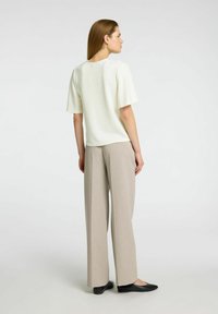 Elfenbensfärgad kortärmad topp med rund halsringning, matchad med beige vida byxor och svarta ballerinas, visad bakifrån.