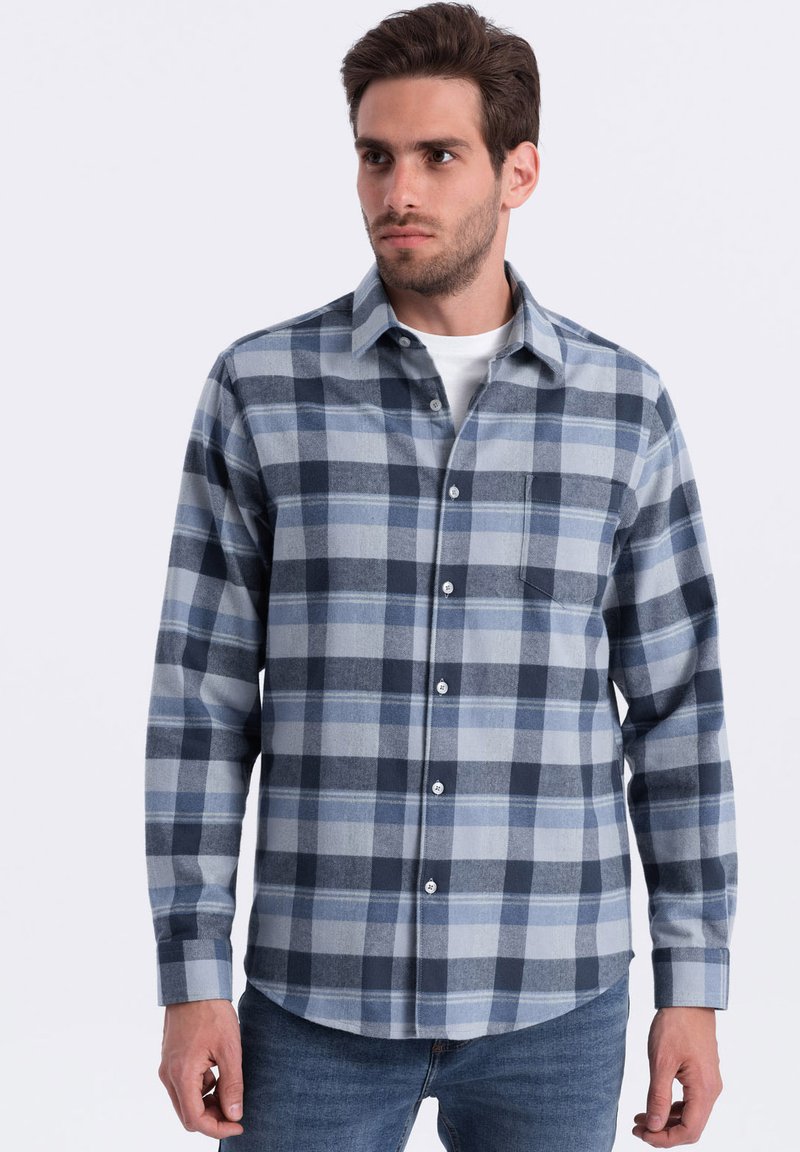 Camisa de franela con un patrón de cuadros en azul y gris claro, con botones frontales, cuello y un bolsillo en el pecho. Mangas largas con puños de botón.