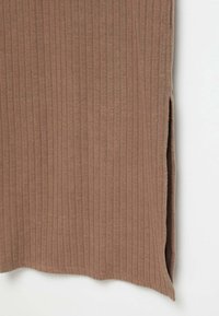 Gros plan sur l'ourlet d'une jupe en tissu côtelé marron avec une fente latérale sur fond blanc.