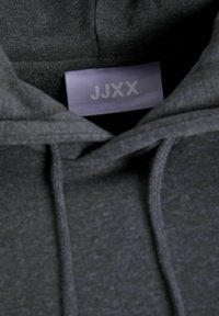 Mørk grå hettegenser med myk tekstur, snor og en rektangulær etikett med "JJXX" i lys grå.