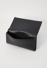 Clutch in pelle nera con una texture liscia, si apre per rivelare un unico scomparto e un'etichetta interna. Presenta una chiusura a pressione circolare.