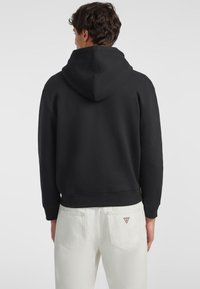 Felpa con cappuccio nera con polsini e orlo a coste, abbinata a pantaloni bianchi con un piccolo etichetta logo sulla tasca posteriore.