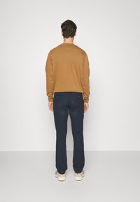 Felpa marrone e pantaloni blu scuro visti da dietro. La felpa ha un colletto a girocollo; i pantaloni sono aderenti con una leggera texture e orli risvoltati.