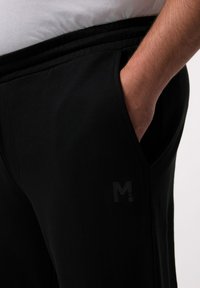 Schwarze Sweatpants mit elastischem Bund, Seitentaschen und einem dezenten Logo auf dem Oberschenkel. Aus weichem, dehnbarem Material gefertigt.