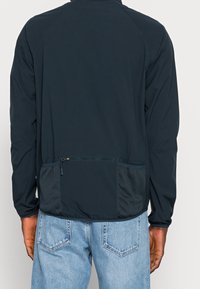 Námořnický větruodolný kabát s dlouhými rukávy, síťovou boční kapsou a kapsou na zip na zadní straně; lehká, hladká tkanina s přiléhavým střihem.