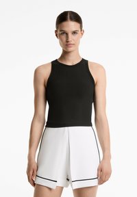 Svart ribbad linne med hög hals och ärmlös design, parat med vita shorts med svart kant och strukturerad form.