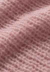 Miękka, różowa dzianina o teksturowanej, puszystej powierzchni. Charakteryzuje się luźnym splotem, co zwiększa jakość dotykową i głębię wizualną.