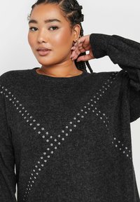 Maglione oversize grigio scuro realizzato in tessuto morbido, con accenti a borchie disposti in un motivo diagonale sulla parte anteriore e maniche lunghe e rilassate.
