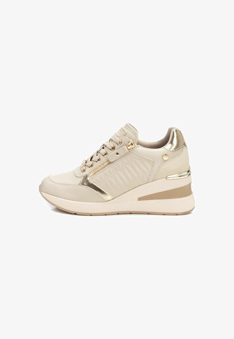 Zapatilla beige con un brillante acento dorado, que presenta un lateral texturizado, un zipper decorativo y una suela tipo cuña para mayor elevación.