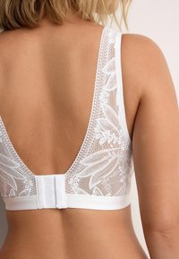 Weißes Spitzen-Bralette mit tiefem V-Ausschnitt, Blumenmuster, satiniertem Unterband und verstellbarem Haken- und Ösenverschluss. Strukturiertes Spitzen-Detail.